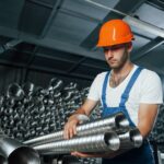 Takes ventilation pipes. Man in uniform works on the production. Industrial modern technology