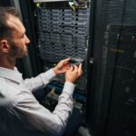 Handsome Caucasian system administrator controlling operational server rack in room indoors